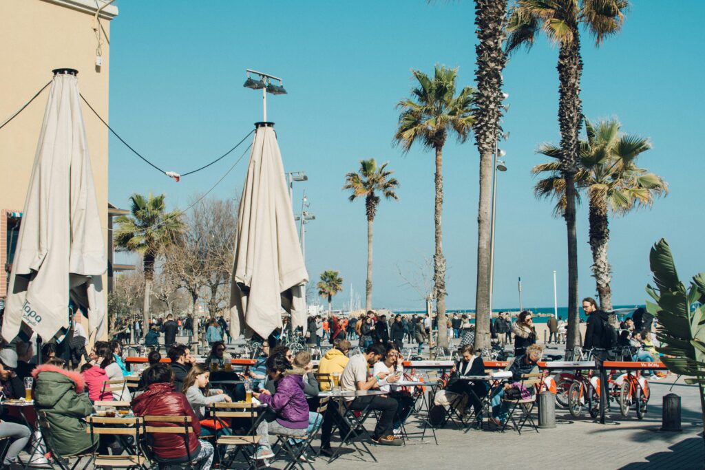 Colorful outdoor cafe in Barcelona with people enjoying a sunny day by the beach.